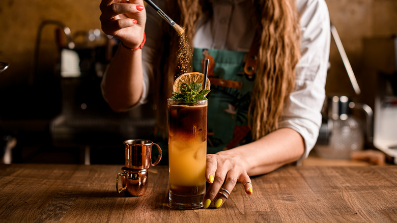 A barista garnishes a drink with cinnamon
