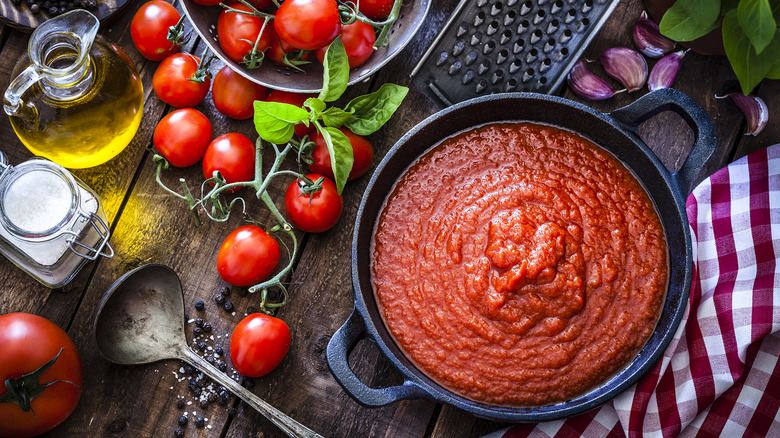Red tomato sauce in a pot surrounded by ingredients