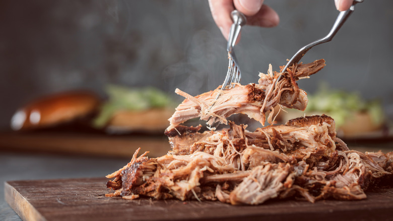pulled pork being shredded on cutting board