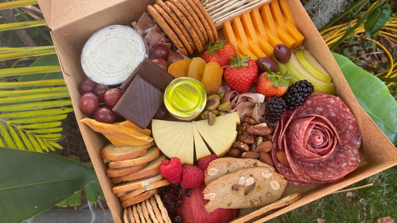 Variety of charcuterie in a box, including salami, chocolate, fruit, crackers, and cheese