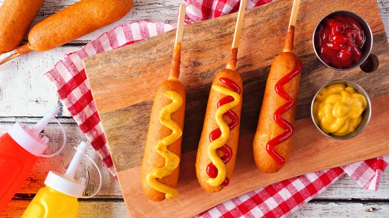 Ketchup and mustard-covered corn dogs on a wooden plank