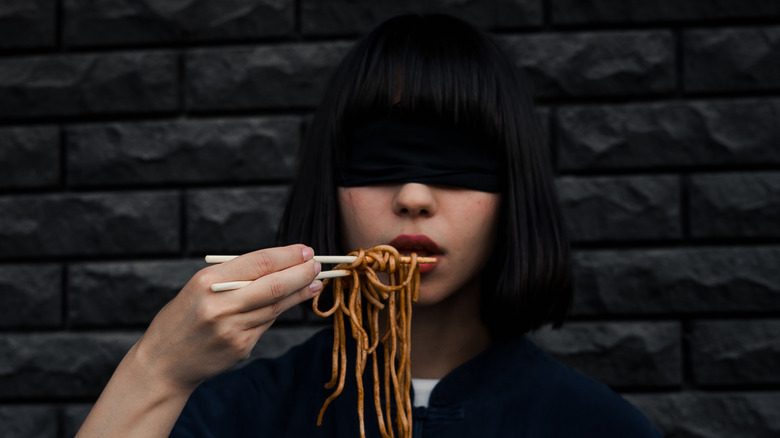 woman eating noodles while blindfolded