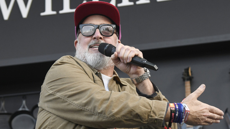 Andrew Zimmern talking into a microphone gesturing to something beside him on stage