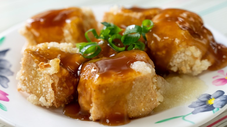 Pieces of fried stinky tofu with a glaze and green onions on top.