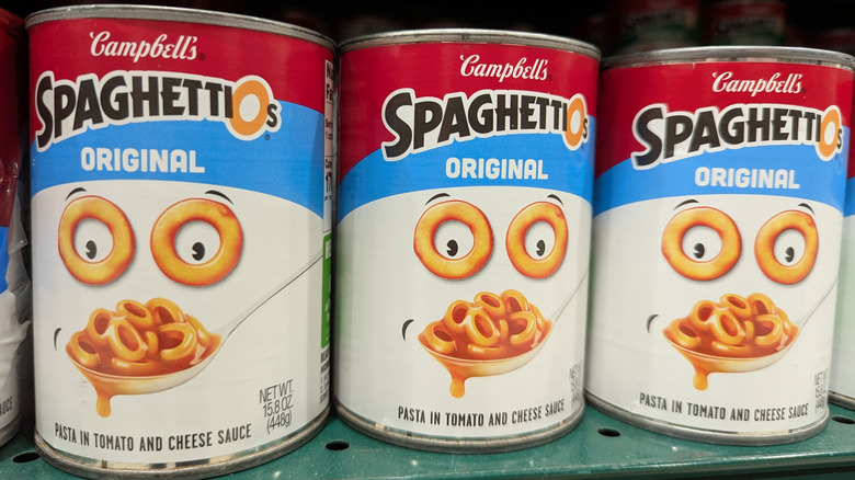 Cans of Campbell's SpaghettiOs on a green metal shelf
