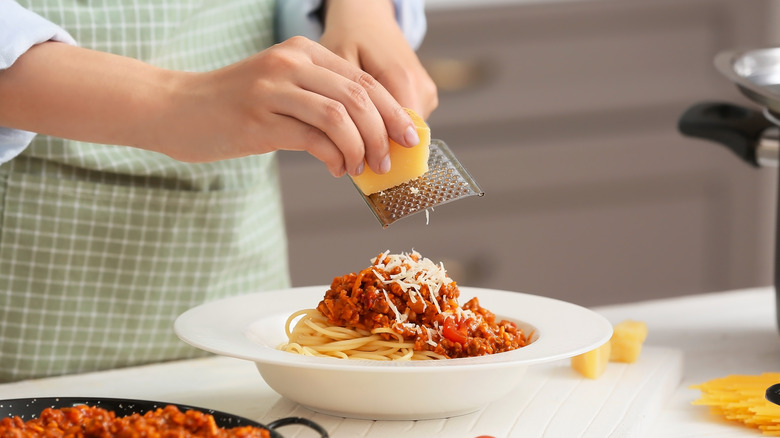 Hands grating cheese onto pasta