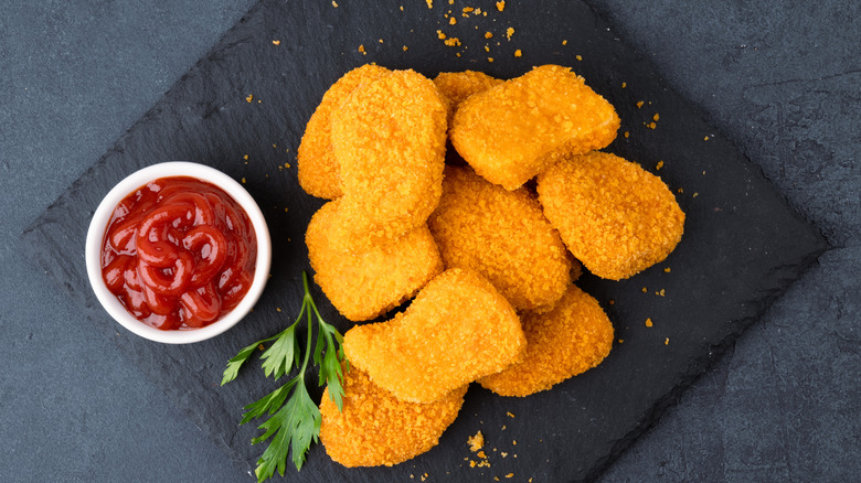 A plate of chicken nuggets with ketchup in a smaller bowl