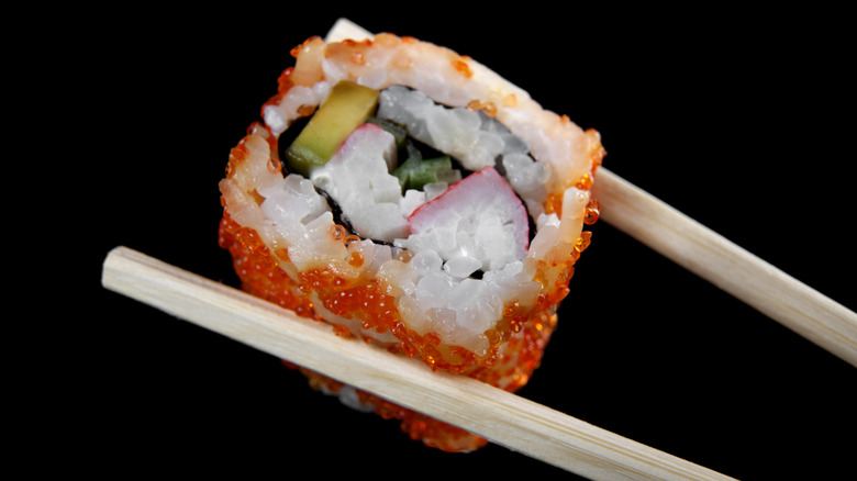 Person holding California roll with chopsticks