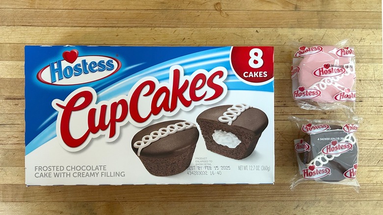 Box of chocolate Hostess CupCakes next to two cupcakes in wrappers