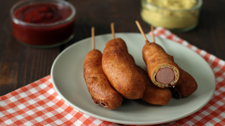 A plate of corn dogs, with sauces behind them