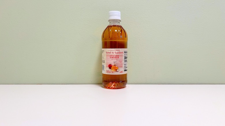 Bottle of Bowl & Basket apple cider vinegar on a white tabletop against a pale green wall.