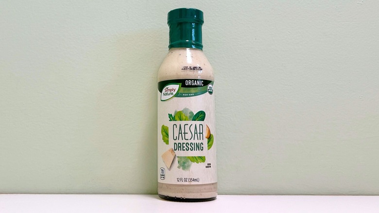 A bottle of Aldi's Simply Nature orangic Caesar salad dressing against a light green wall