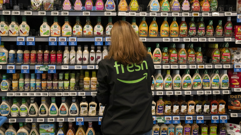An Amazon fresh employee inspecting bottles of salad dressing in a grocery store