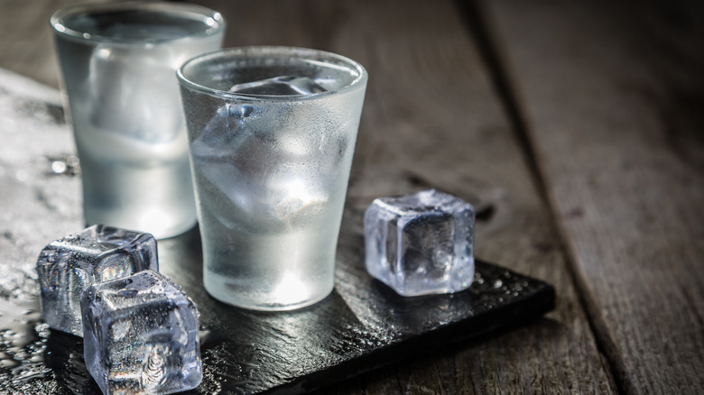 two shots of vodka with ice on wooden board