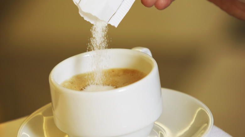 pouring sugar packet into white coffee cup on saucer