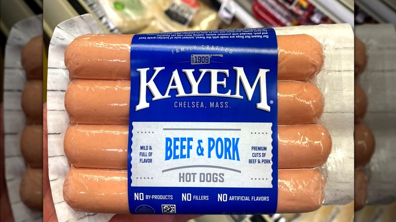 Shopper holding package of Kayem beef and pork hot dogs in grocery store