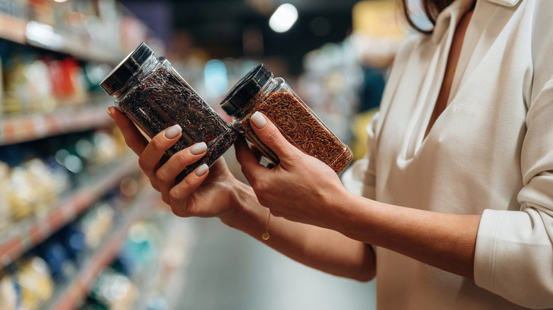 Close-up on a customer's hands holding two unlabeled spice canisters to compare them