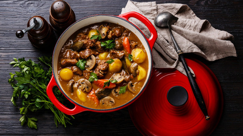Beef stew in a Dutch oven with a ladle, parsley, and salt and pepper shakers