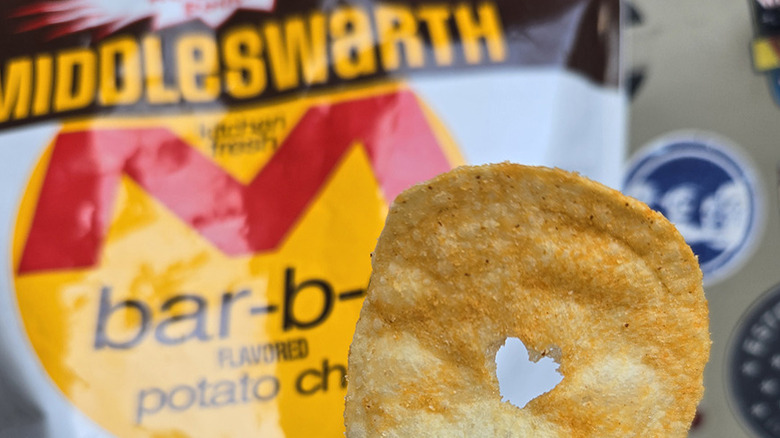 Potato chip with heart cut-out in it, held against Middleswarth chip bag