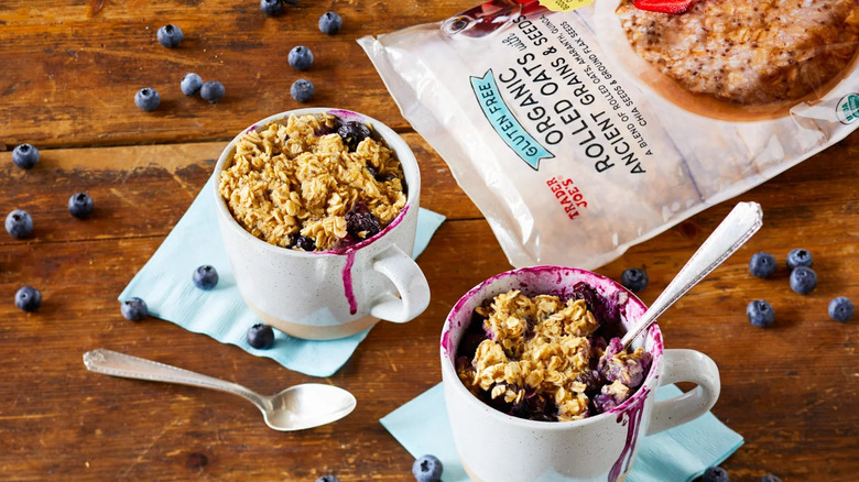 Bag of Trader Joe's rolled oats next to two mugs of oat bowls with blueberries scattered around table
