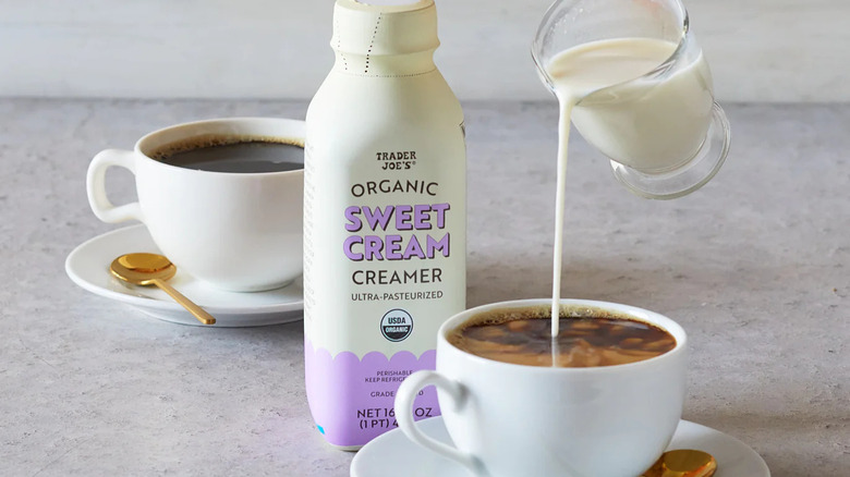 Bottle of Trader Joe's sweet cream coffee creamer next to coffee mugs with creamer being poured in