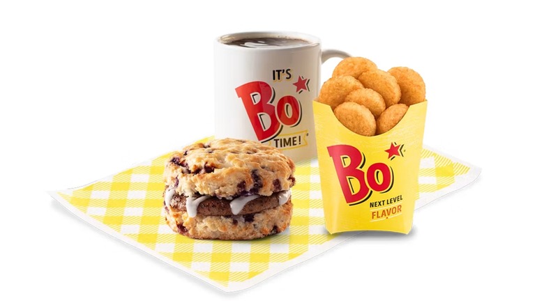 Bojangles Sausage Bo-Berry biscuit with Bo-Tato Rounds and coffee in a slogan-themed cup on a white background