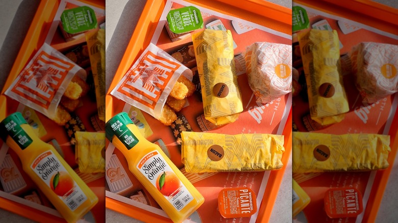 Whataburger tray of wrapped breakfast burritos and a biscuit with Simply orange juice and hash brown sticks
