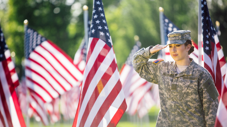 U.S. soldier in military fatigues saluting while surrounded by several American flags