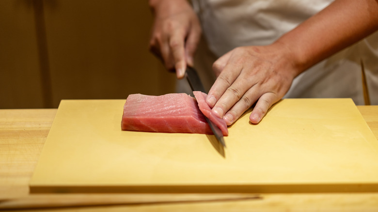 A chef gently cutting raw tuna on a wooden cutting board
