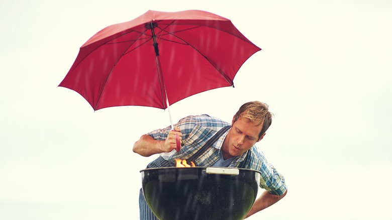 man grilling in rain with umbrella