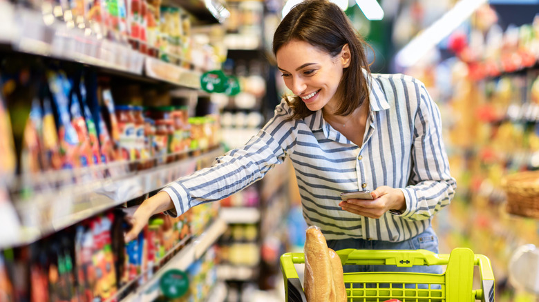 A woman pulling something off the grocery shelf and putting into a yellow cart