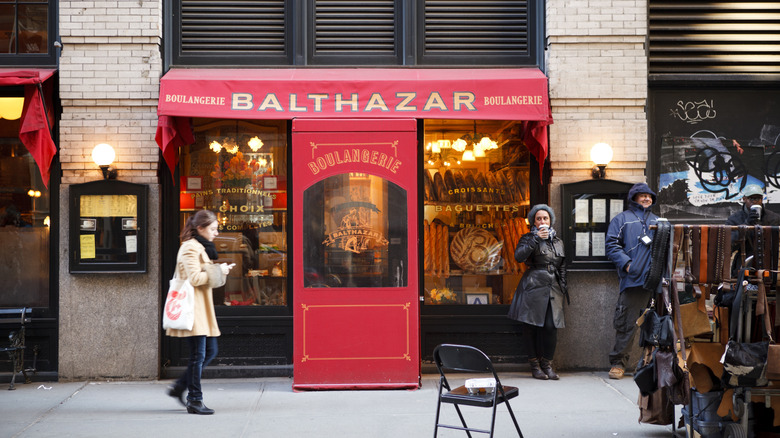 The outside of Balthazar restaurant in NYC with a red awning and customers walking past