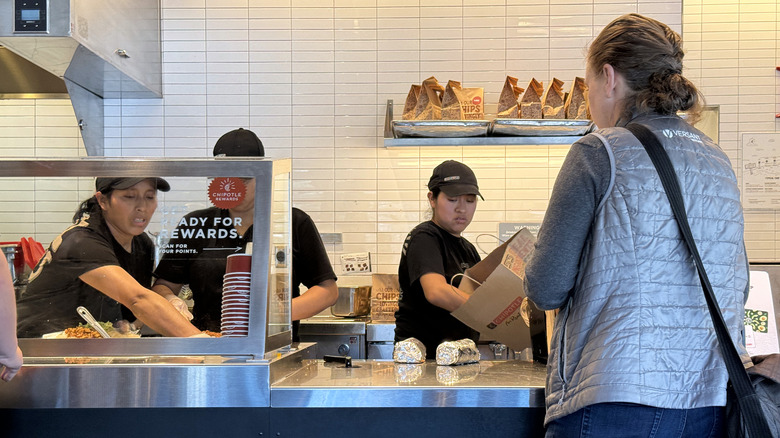 A woman waiting at the cash register at Chipotle with employees looking busy
