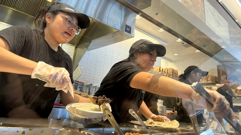 Chipotle employees preparing various orders in a line