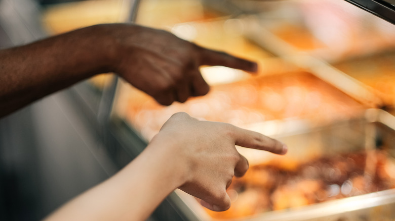 Two customers pointing at food over the sneeze guard