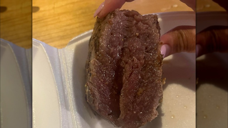 A hand holds an overcooked steak from Logan's Roadhouse