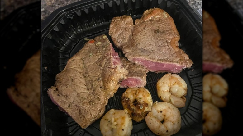 An undercooked Ruby Tuesday ribeye and shrimp in a takeout container
