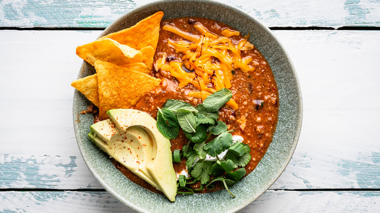 Chili with tortilla chips, avocado, cheese, and herbs