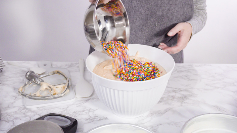 A person mixing in sprinkles to a bowl of cake batter to make funfetti