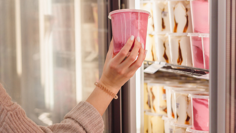 Person taking pink ice cream from grocery store freezer