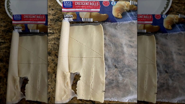 torn aldi crescent roll dough on a granite countertop with the package nearby.