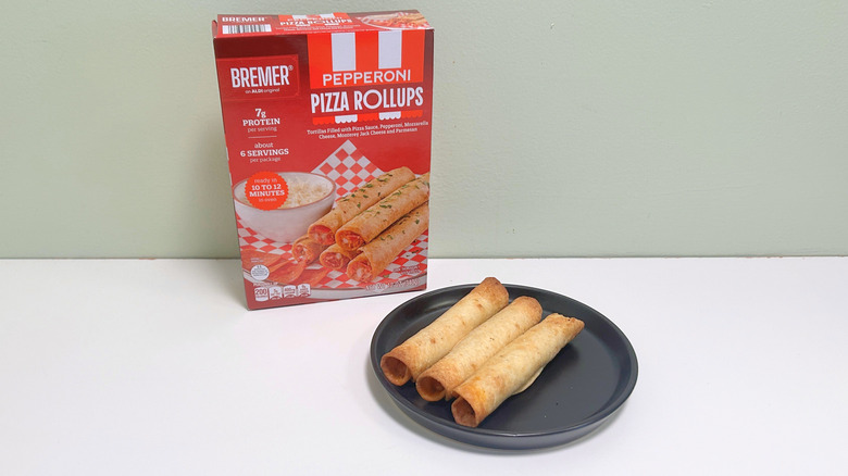 A box of Bremer Pepperoni Pizza Rollups next to pizza rollups on a black plate