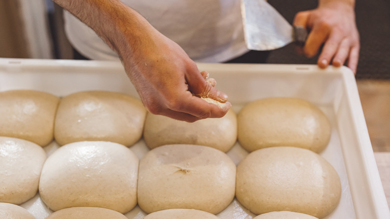 Balls of fresh pizza dough with a hand above them holding a piece of dough
