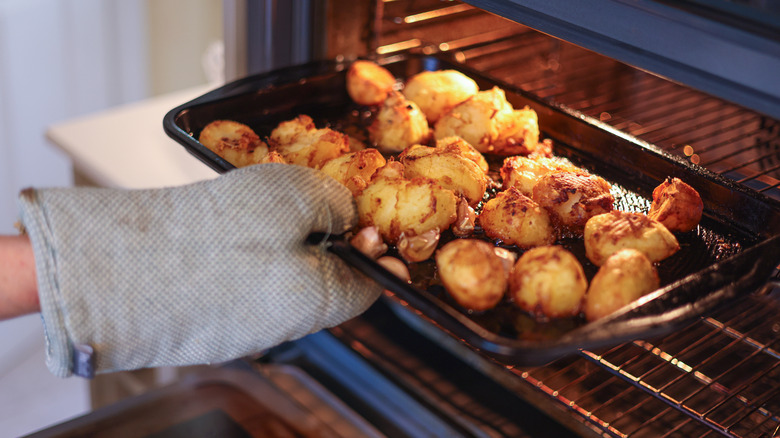 A hand in an oven mitt taking a pan of crispy potatoes out of an oven