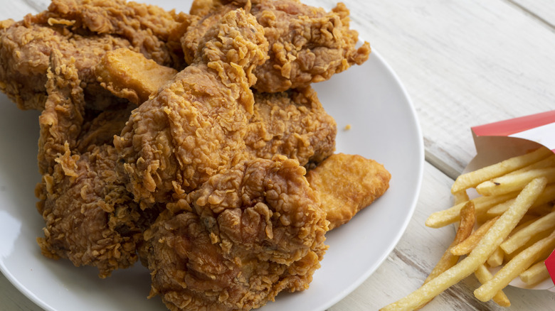 Several pieces of fried chicken piled on a white plate with fries