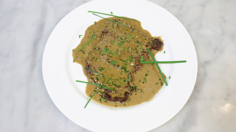White-plated steak Diane with sprinkle of herb on top