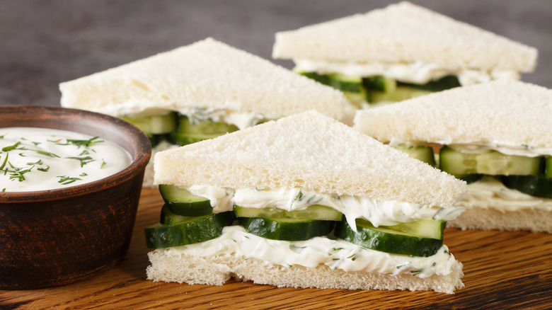 Four cucumber and cream cheese sandwiches on a wooden board