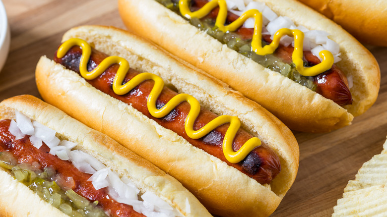 Hot dogs in buns with relish, white onions, and yellow mustard