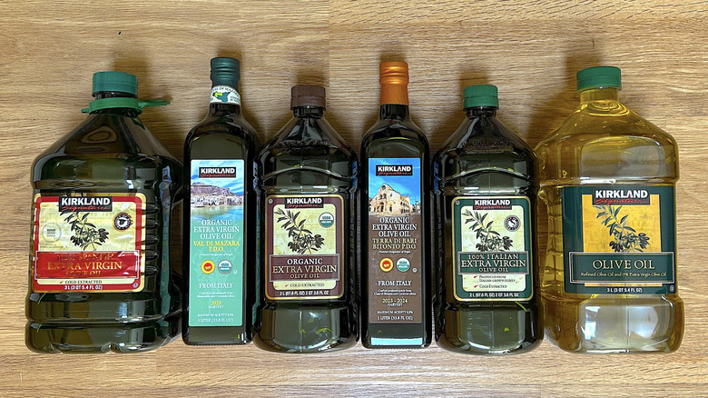 Six different bottles of Kirkland olive oil on a wood background