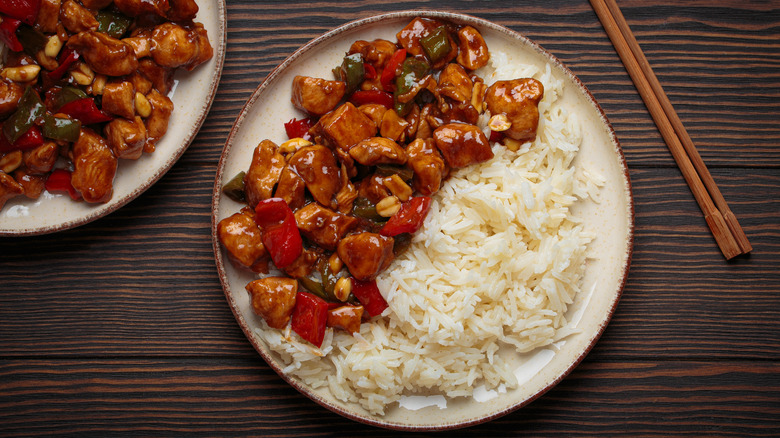 plate with kung pao chicken and rice, next to chopsticks